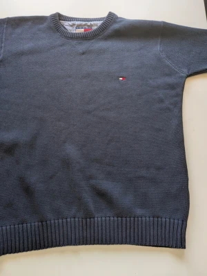 Tommy Hilfiger tjock tröja - Mörkblå stickad tröja från Tommy Hilfiger med rund halsringning och diskret logga broderad på bröstet. Tröjan har ribbade muddar vid ärmslut och nederkant. Klassisk och enkel design som passar till mycket. Materialet känns mjukt och bekvämt.
