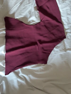 Vinröd oneshoulder topp - Trendig vinröd topp med oneshoulder-design och lång ärm. Snygg asymmetrisk form som ger en cool och modern look. Perfekt att styla med jeans eller kjol för en stilren outfit.