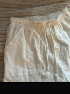 Vita mjukisbyxor med dragsko - Säljer ett par vita mjukisbyxor med resår i midjan och dragsko för skön passform. Byxorna har två sidofickor och är tillverkade i ett mjukt och bekvämt material. Perfekta för chill dagar hemma eller när du vill ha det extra comfy.