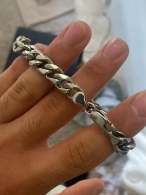 Tungt silverfärgat kedjearmband - Säljer ett stilrent och chunky armband i silverfärgad metall med breda, platta länkar. Perfekt för dig som gillar en clean och modern look. Länkarna har en blank finish och armbandet har ett rejält spänne som håller det på plats.