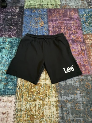 Svarta shorts från Lee - Svarta shorts från Lee med elastisk midja och vit logga på vänster ben. Klassisk och enkel design, perfekta för sommaren. Tillverkade i mjukt material som känns bekvämt hela dagen.