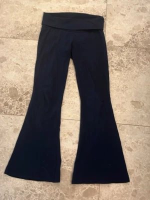 Marinblå bootcut leggings/yogapants RYVLS - Säljer ett par marinblå bootcut leggings från RYVLS med bred midjeresår och utsvängda ben. Det står Stockholm på baksidan. Mjukt och stretchigt material som sitter skönt på kroppen. Perfekta för en avslappnad och trendig look.