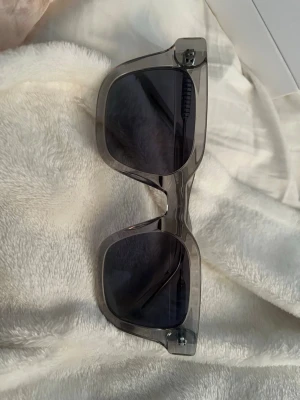 Transparenta solglasögon med rund form - Snygga solglasögon med transparent båge och rundade glas. Glasögonen har en modern och stilren design som passar perfekt till dig som gillar en clean look. Bågarna är i plast och känns lätta att bära.