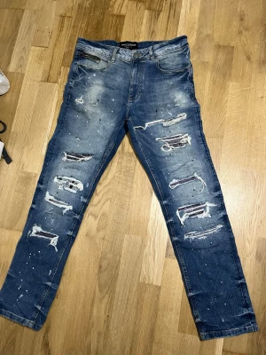 Blå slitna jeans med hål - Säljer ett par blå jeans från Only & Sons med kraftiga slitningar och hål på både fram- och baksida. Jeansen har en skinny fit och detaljer med färgstänk för en trendig, avslappnad look. Klassisk femficksmodell och knappgylf.