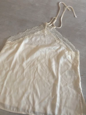 Krämfärgat nattlinne med spets - Sött linne i krämfärgad satin med tunna axelband och spetsdetaljer vid bysten. Lätt och luftigt material som känns mjukt huden. 