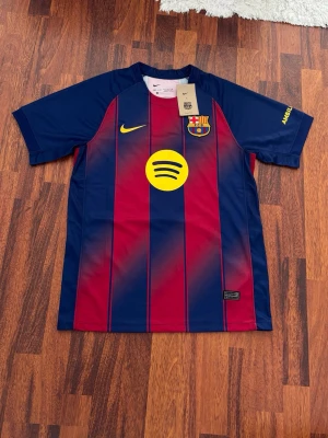FC Barcelona matchtröja Nike - Snygg FC Barcelona matchtröja från Nike med klassiska blå och röda vertikala ränder. Tröjan har klubbmärke på bröstet, gul Nike-logga och Spotify som sponsor framtill. Tillverkad i lätt och ventilerande material, perfekt för fotboll eller träning. På ryggen är det lamine yamal 10