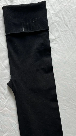 Victoria’s Secret PINK Seamless Capri Yoga Pants  - Säljer ett par svarta leggings från PINK med hög midja och bred linning där loggan syns diskret framtill. Stretchigt material som sitter skönt och följsamt. Perfekta till en avslappnad stil eller när du vill vara bekväm hela dagen.