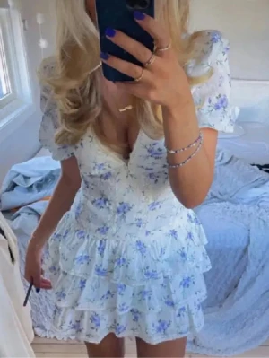 Zara Vit blommig volangklänning klänning Stl s  - Supersöt kort klänning i vitt med lila och blått blommönster. Puffärmar, v-ringning och flera lager volanger i kjolen ger en romantisk vibe. Perfekt för sommarens alla tillfällen. 