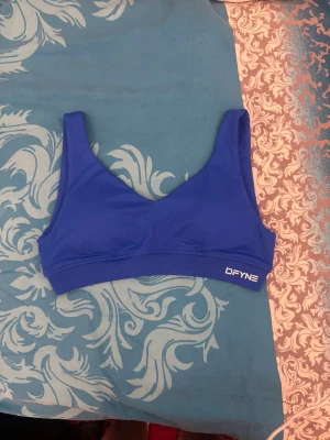Blå sport-bh från DFYNE - Snygg blå sport-bh från DFYNE med breda axelband och elastisk resår under bysten. Tillverkad i ett stretchigt material som ger bra stöd och komfort. Perfekt för träning eller chill dagar. Logga framtill och enkel, stilren design.