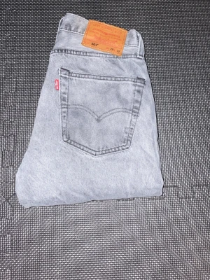 Levi's 501 ljusgrå jeans - Säljer ett par klassiska Levi's 501 jeans i ljusgrå tvätt. Jeansen har rak passform, fem fickor och den ikoniska röda Levi's-lappen på bakfickan. Tillverkade i slitstark denim med läderpatch bak i midjan. Perfekta för en avslappnad och trendig look. W28 L32