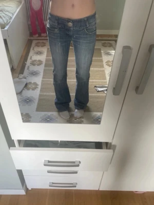 Sisters point - Säljer ett par blå bootcut jeans med låg midja och klassiska fem fickor. Jeansen har ljusa slitningar och kontrastsömmar för en snygg vintagekänsla. Perfekta för dig som gillar en avslappnad och trendig stil.