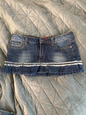 Blå jeanskjol med volang och frans - Snygg blå jeanskjol med volangkant och fransdetalj.        W: 29 L:32