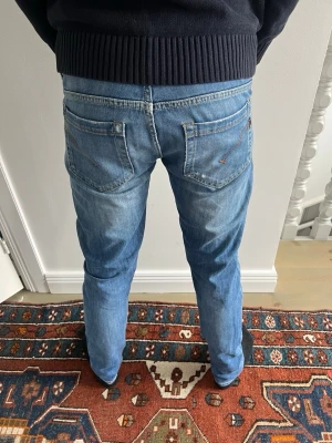 Blå slim fit jeans med slitningar dondup - Säljer ett par ljusblå slim fit jeans med snygga slitningar. Jeansen har klassiska fem fickor och normal midja. Perfekta för en avslappnad och trendig look. Materialet är mjukt denim i bomull.självklart äkta