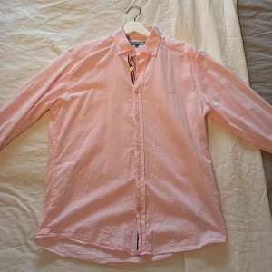 Ljusrosa linneskjorta från Edoardo Caravella - Säljer en ljusrosa linneskjorta från Edoardo Caravella med klassisk krage och långa ärmar. Skjortan har knappar framtill och en snygg randig detalj på insidan av knappslån. Perfekt för en stilren och avslappnad look.