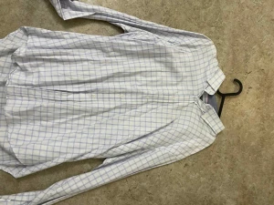 Vit rutig skjorta med blå rutor - Klassisk vit skjorta med tunna blå rutor och knappar framtill. Skjortan har lång ärm och en avslappnad passform. Perfekt till jeans eller chinos för en clean och stilren look.