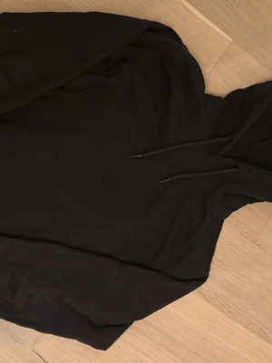 Svart hoodie från Jack & Jones - Snygg svart hoodie från Jack & Jones med klassisk huva och dragsnören. Hoodien har en stor magficka framtill och är tillverkad i mjukt material som känns skönt mot huden. Perfekt för en avslappnad och stilren look. Nypris: 400, använd max 3 ggr så den är gott som ny