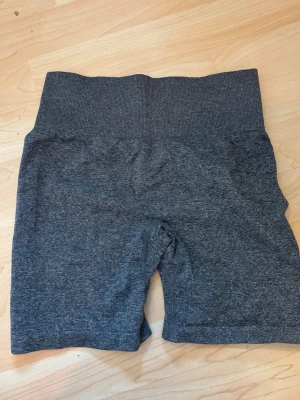 Mörkgrå träningstights shorts - Mörkgrå, högmidjade träningstights shorts från Strength. Tillverkade i ett stretchigt syntetmaterial som sitter tight och bekvämt. Perfekta för gymmet eller annan träning. Breda resår i midjan för extra stöd.