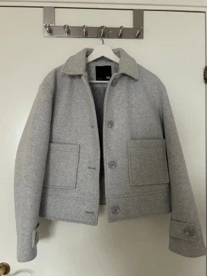 Ljusgrå jacka  - Stilren ljusgrå jacka från lager 157 med klassisk krage och stora framfickor. Jackan har stora knappar framtill och på ärmsluten. Jackan är oanvänd. Jackan är i storlek XS men sitter som en S. 