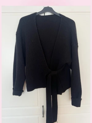 Svart stickad kofta med knytband - 💕Mysig svart stickad kofta med långa ärmar och breda ribbade muddar. Koftan har ett knytband i midjan som ger en snygg siluett och öppen front. Perfekt att slänga över en topp för en avslappnad look.💓den blir omlott 