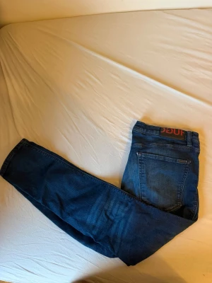 Mörkblå jeans från Hugo - Snygga mörkblå jeans från Hugo med klassisk femficksdesign och rakt ben. Jeansen har en tydlig Hugo-logga i rött på bakre läderpatchen och är tillverkade i mjuk denim. Perfekta för dig som gillar stilrena och moderna jeans.