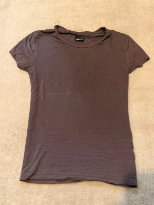 Mörkbrun basic t-shirt från Gina Tricot - En enkel och stilren mörkbrun t-shirt från gina med rund halsringning och korta ärmar. Tillverkad i mjuk bomull som känns skön mot huden. Perfekt att matcha med jeans eller kjol för en clean look.