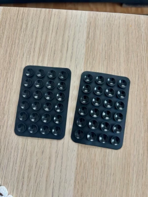 Octopus Två Svarta sugproppsmattor till mobil - Två svarta Octopus silikon rektangulära sugproppsmattor i mjukt gummi, perfekta för att fästa mobilen på släta ytor. Varje matta har flera små sugproppar. Smidig lösning för handsfree-användning eller i bilen. Nya