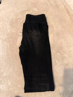 Svarta raka jeans - Säljer ett par svarta jeans med rak passform och klassisk femficksdesign. Jeansen har knappgylf och bälteshällor. Materialet är denim med lätt stretch för extra komfort. Perfekta till en avslappnad stil.