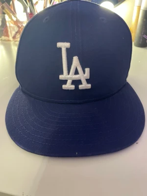 Blå LA Dodgers keps - Snygg blå keps från New Era med LA Dodgers-logga broderad i vitt framtill. Klassisk modell med böjd skärm och ventilationshål. Perfekt för dig som vill ha en sportig och trendig look. Materialet är tålig bomull som andas.