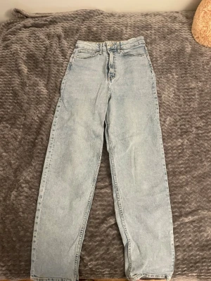 H&M Ljusblå raka jeans med hög midja  - Säljer ett par ljusblå jeans med rak passform och hög midja. Jeansen har klassisk femficksdesign och stängs med dragkedja och knapp. Perfekta för en avslappnad och trendig look. Materialet är denim i bomull.