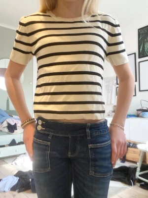 Randig kortärmad topp från Gina Tricot - Säljer en snygg kortärmad topp från Gina Tricot i vitt med svarta horisontella ränder. Toppen har en rund halsringning och är gjord i mjuk bomull. Perfekt till jeans eller kjol för en enkel och trendig look.❤️