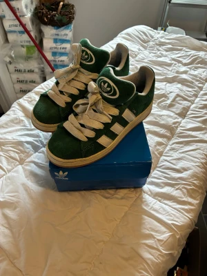 Gröna Adidas campus 00  - Snygga gröna Adidas campus 00 sneakers i mocka med vita detaljer och breda vita skosnören. Klassisk låg modell med de ikoniska tre ränderna på sidan och stor Adidas-logga på plösen. Skorna är i princip nya, användna nån gång men inget som syns. Köpta förra året hos zalando. 