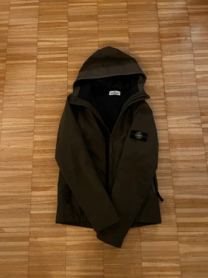 Stone Island vindjacka - Snygg mörkgrön vindjacka från Stone Island med huva och dragkedja. Jackan har en klassisk patch med logga på vänster ärm och två sidofickor med dragkedja. Jag själv är 175cm 70kg och ör lite för liten men passar endå skulle rekommendera att man är någonstans 165-170 för en perfekt passform