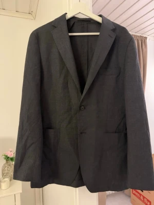 Mörkgrå klassisk kavaj - Stilren mörkgrå kavaj med två framfickor och en bröstficka. Enkelknäppt modell med smala slag och rak passform. 