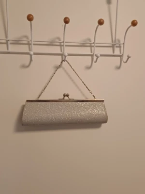 Glittrig silver kuvertväska - Säljer en glittrig silverfärgad kuvertväska med metallkedja och klassiskt klolås. Väskan har en avlång och elegant form, perfekt för att bära det viktigaste. Märke vet ej, skriv om ni har frågor, priset går att diskutera ❤️