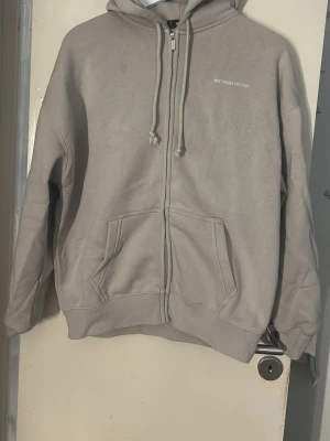 Ljusgrå oversized zip hoodie från Stringtstyr - Ljusgrå hoodie med dragkedja från Stringtstyr. Klassisk modell med huva och justerbara snören, samt två stora fickor framtill. Tillverkad i mjukt material som känns skönt mot huden. Perfekt för en avslappnad och stilren look. Storlek xxs är som M/L