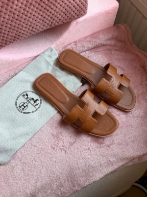 H Oran sandaler  - Säljer ett par klassiska Oran sandaler i brun färg. Sandalerna har den ikoniska H-designen över foten. Liten i storlek så detta är en strl 37