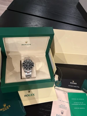 Submariner silver klocka - Säljer en stilren Submariner med svart urtavla och silverfärgat armband i rostfritt stål. Klockan har klassisk rund form, tydliga markeringar och vridbar bezel. Kommer med originalbox, certifikat och tillbehör.