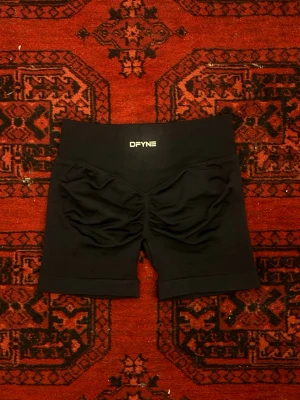Svarta träningstights från DFYNE - Säljer ett par svarta, högmidjade träningstights från DFYNE. Shortsen har en tight passform och snygg scrunch-detalj bak för extra form. Perfekta för gymmet eller andra träningspass.