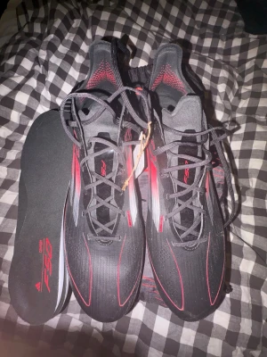 Adidas F50 Elite FG fotbollsskor - Snygga Adidas F50 Elite FG fotbollsskor i svart med röda och silverfärgade detaljer. Skorna har en modern, strömlinjeformad design och är tillverkade i syntetmaterial för lätt vikt och bra bollkontroll. Perfekta för spel på naturgräs och för dig som vill sticka ut på planen.