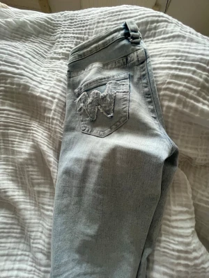 Ljusblå jeans från Gina Tricot - Säljer ett par ljusblå jeans från Gina tricot  med klassiska fickor och det ikoniska W-broderiet på bakfickan. Jeansen har bootcut ben och bälteshällor. Materialet är mjukt denim i bomull, perfekt för en avslappnad stil.Low waist