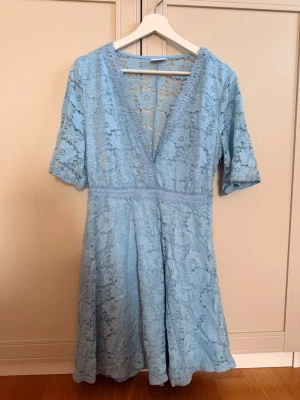 Ljusblå spetsklänning från Vila - Superfin ljusblå klänning från Vila med v-ringning och spetsdetaljer. Klänningen har kort ärm, markerad midja och vackert blommigt spetsmönster. Små små slitningar på spetsen kan förekomma men ingenting som syns 