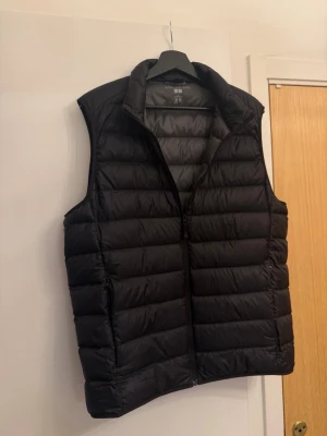 Svart dunväst från Uniqlo - Stilren svart dunväst från Uniqlo med quiltad design och hög krage. Inga skador eller skavanker alls, den är i nyskick!