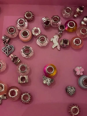 Charmarmband med färgglada pärlor - Charmarmband med flera pärlor i olika färger som rosa, orange, blå och silver. Pärlorna har olika former och mönster, vissa är glittriga och andra har ränder eller metallinslag. Perfekt för dig som gillar att mixa och matcha detaljer.