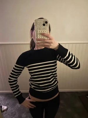 Svartvit randig stickad tröja - Säljer en snygg stickad tröja med svarta och vita horisontella ränder. Tröjan har rund hals och långa ärmar med ribbade muddar. Perfekt för dig som gillar klassiska mönster och enkel stil.