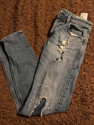 Blå slitna jeans från diesel - Säljer ett par blå jeans med slitningar och hål på framsidan för en trendig, avslappnad look. Jeansen är ljusblå och riktigt sköna. Storlek 29/30 pris går att diskutera vid snabb affär🙌