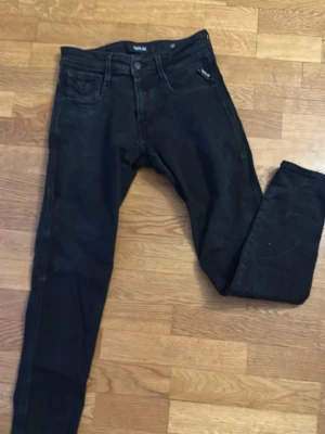 Svarta slim fit jeans från Replay - Snygga svarta jeans från Replay i slim fit-modell (Anbass). Klassisk femficksdesign med dragkedjegylf och bälteshällor. Materialet är stretchigt för extra komfort. Storleken är w28 l30