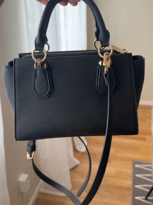 Svart handväska från Zalando - Snygg svart handväska från Zalando med guldfärgade detaljer och strukturmönstrat konstläder. Väskan har både handtag och justerbar axelrem, samt dragkedja upptill. Perfekt storlek för det viktigaste och stilren design som passar till många outfits.