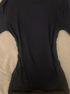 Mörkblå topp från Gina Tricot - En enkel och stilren mörkblå topp från Gina Tricot. Modellen har rund halsringning och är tillverkad i ett mjukt material som sitter bekvämt mot kroppen. Perfekt att matcha med jeans eller kjol för en clean look.