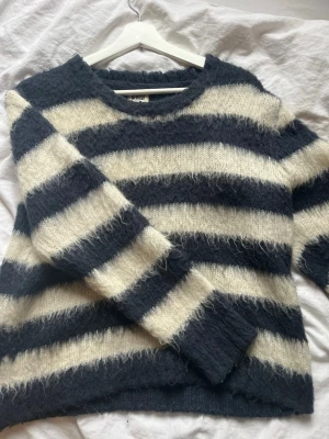 Fin mohair tröja från Weekday - Mysig mohair tröja från Weekday med breda svarta och vita ränder. Tröjan har en fluffig, lite luddig textur och rund halsringning. Perfekt för kalla dagar och enkel att styla med jeans eller kjol.