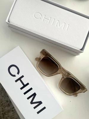 Beige CHIMI solglasögon - Snygga solglasögon från CHIMI med beige transparenta bågar och mörka glas. Modellen har en klassisk rektangulär form och kommer med originalfodral och box. Perfekt för dig som vill ha en stilren och trendig look.